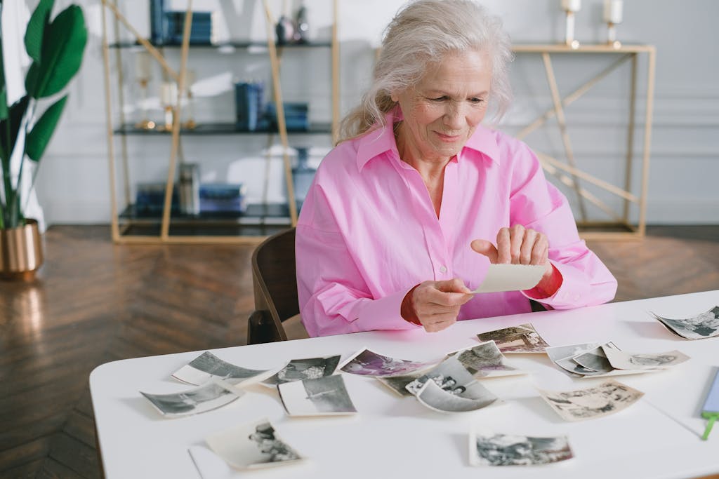 A senior woman reliving past memories by looking through old photographs at a table.