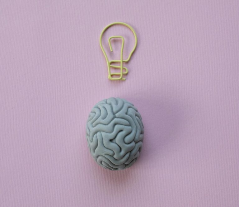 Brain-shaped eraser with a light bulb paperclip on a pastel pink background. Ideal for education and creativity themes.
