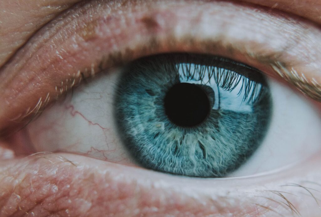 Closeup of crop anonymous person looking at camera with turquoise eye with small black pupil and wavy vessels on eyeball and pale eyelashes with wrinkles on skin