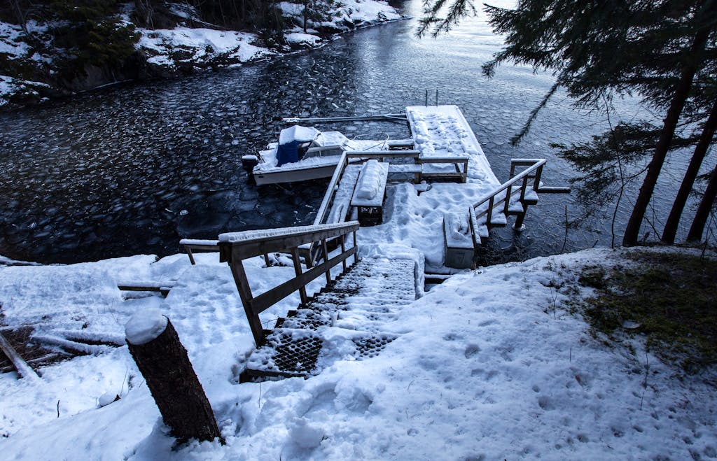 Serene winter scene with snow-covered dock, stairs, and icy water in a tranquil setting.